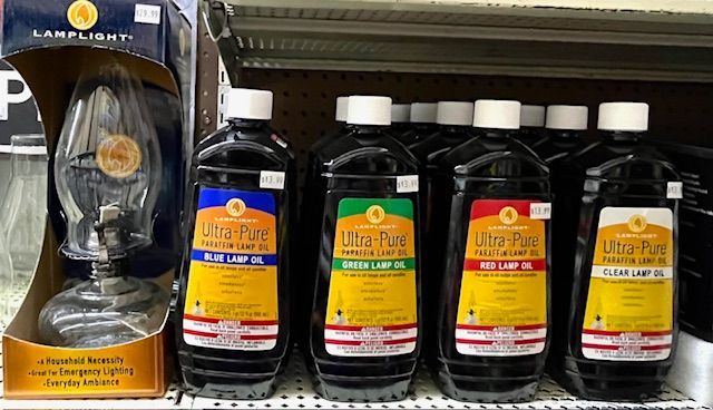 A retail shelf featuring a glass lamp in a box next to four bottles of Lamplight Ultra-Pure colored lamp oil.