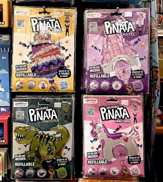Four rectangular packages for inflatable, refillable pinatas in the shapes of a cake, castle, dinosaur, and unicorn.