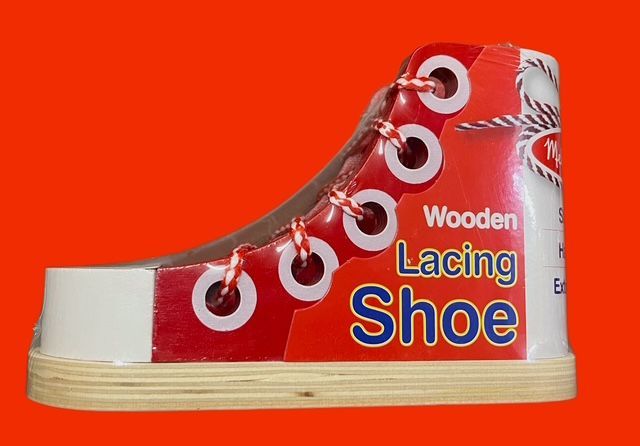 A wooden lacing shoe toy with red sides, white eyelets, and red and white laces against a bright orange background.