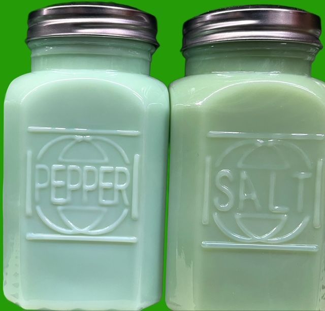 Two vintage-style, light green glass shakers with metal lids, labeled 