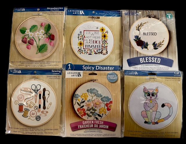 Six different embroidery kits in circular hoops arranged in two rows of three on a black background.
