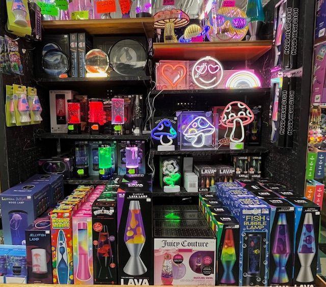 A retail store display shelf packed with colorful lava lamps, neon mushroom signs, and various novelty mood lights.