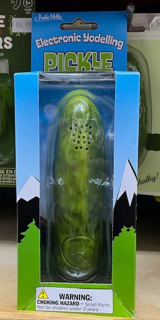 A retail box containing an electronic yodeling pickle toy with a green, bumpy texture on a shelf.