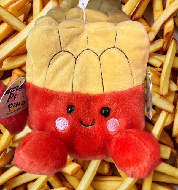 A plush toy shaped like a red box of French fries with a smiling face, resting on a pile of actual fried potatoes.