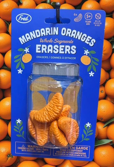 A package of novelty erasers shaped like mandarin orange segments, displayed against a background of fresh oranges.
