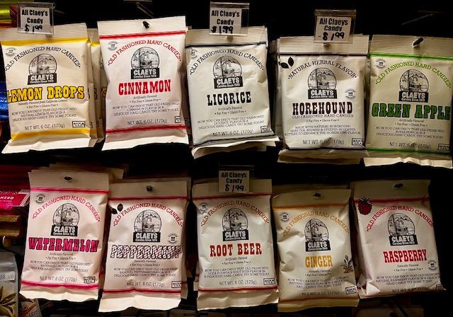 Two rows of Claeys candy bags hanging on store shelves, featuring various flavors like licorice, peppermint, and apple.