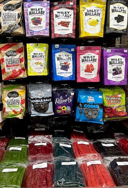A retail display of assorted colorful bags of Wiley Wallaby licorice and various loose candy packages on store shelves.