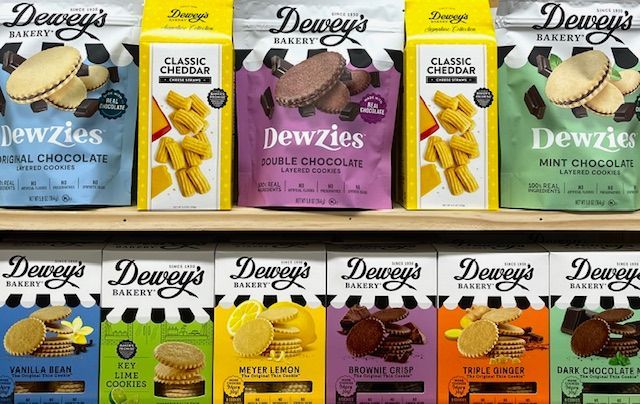 Shelves stocked with various Dewey's Bakery cookies, including Dewzies bags and boxes in many flavors and vibrant colors.