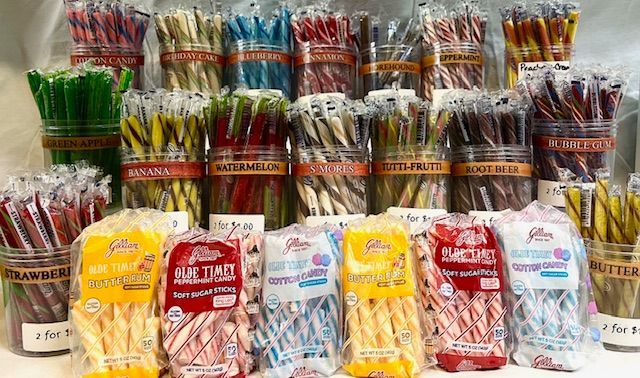 An assortment of colorful candy sticks and wrapped candy bags displayed in clear containers and on a white surface.