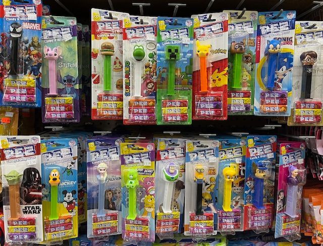 A display of various character-themed PEZ candy dispensers arranged on store shelves.