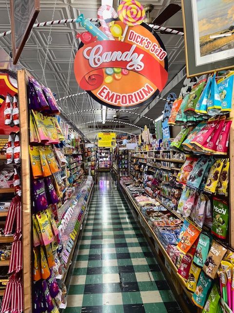 A candy-filled aisle in Dick’s 5 & 10 Emporium, featuring shelves packed with treats and a hanging sign under a tin ceiling.