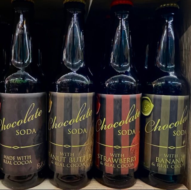 Four bottles of Chocolate Soda in varied flavors—original, peanut butter, strawberry, and banana—lined up on a shelf.