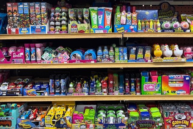 Four shelves in a store aisle filled with colorful children's toys, games, and small character figurines in packaging.