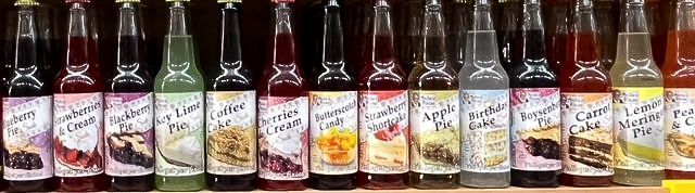 A row of glass bottles containing colorful flavored syrups, each with a label depicting the corresponding dessert flavor.