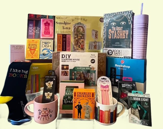 A collection of book-themed gifts, including mugs, a DIY book nook, socks, stationery, and a pink tumbler.