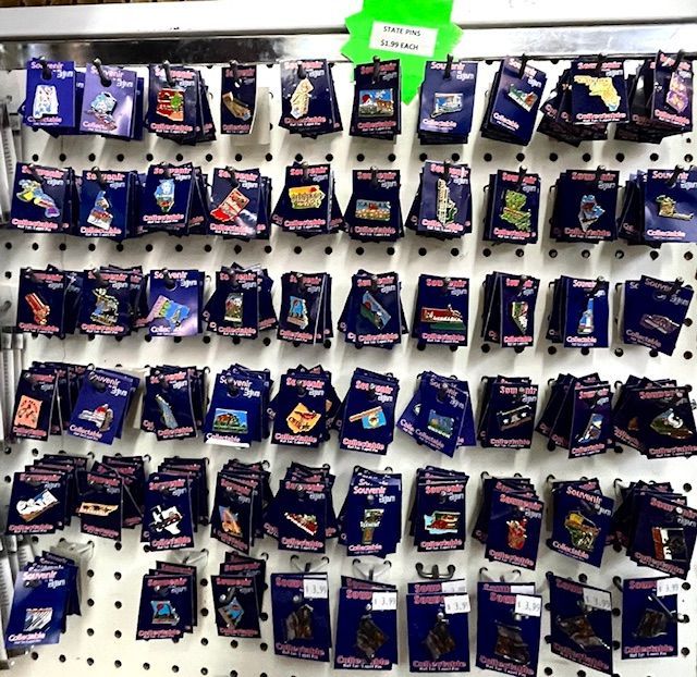 A wall display of numerous souvenir pins packaged on blue cards, arranged in rows on a white pegboard.