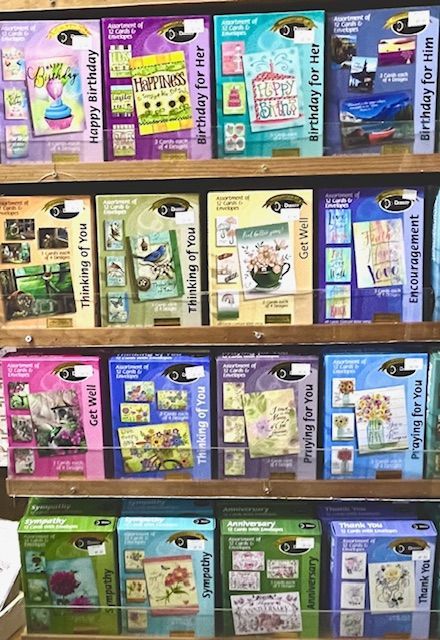 A retail display shelf stocked with rows of boxed greeting cards for various occasions like birthdays, sympathy, and thanks.