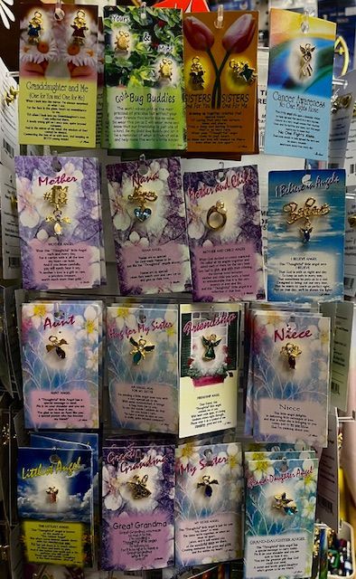 A retail display rack featuring rows of small angel-themed collectible pins on individual cards with floral backgrounds.
