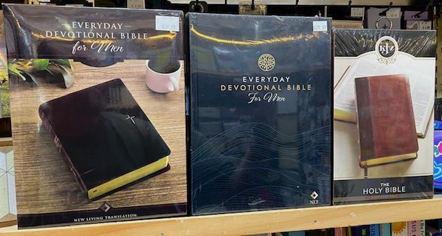 Three boxed Bibles, including two Everyday Devotional Bibles and one Holy Bible, displayed on a wooden shelf.