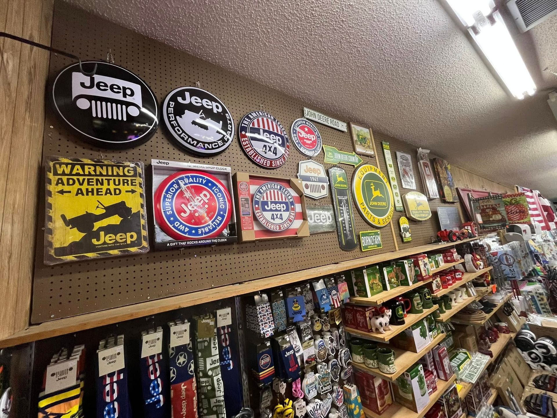 A retail store wall displaying numerous circular and square Jeep-themed metal signs above shelves stocked with merchandise.