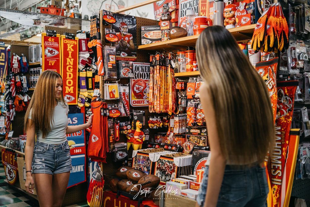Two people browse a store aisle filled with red and yellow Kansas City Chiefs sports merchandise and apparel.