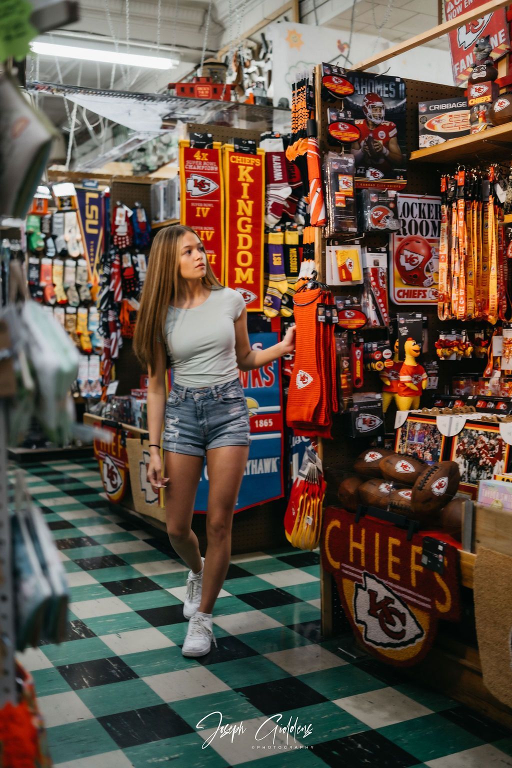 A person standing in an aisle filled with Kansas City Chiefs sports merchandise, wearing a grey shirt and denim shorts.