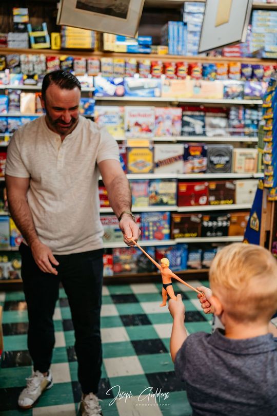 A person and a child stand in a store aisle, playfully stretching a toy figure between them.