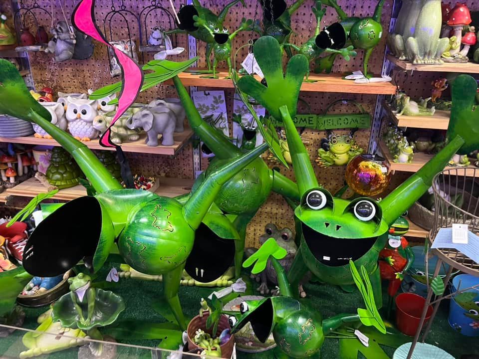 Metal frog garden sculptures in various poses, including two large green frogs with raised arms, on a store shelf.