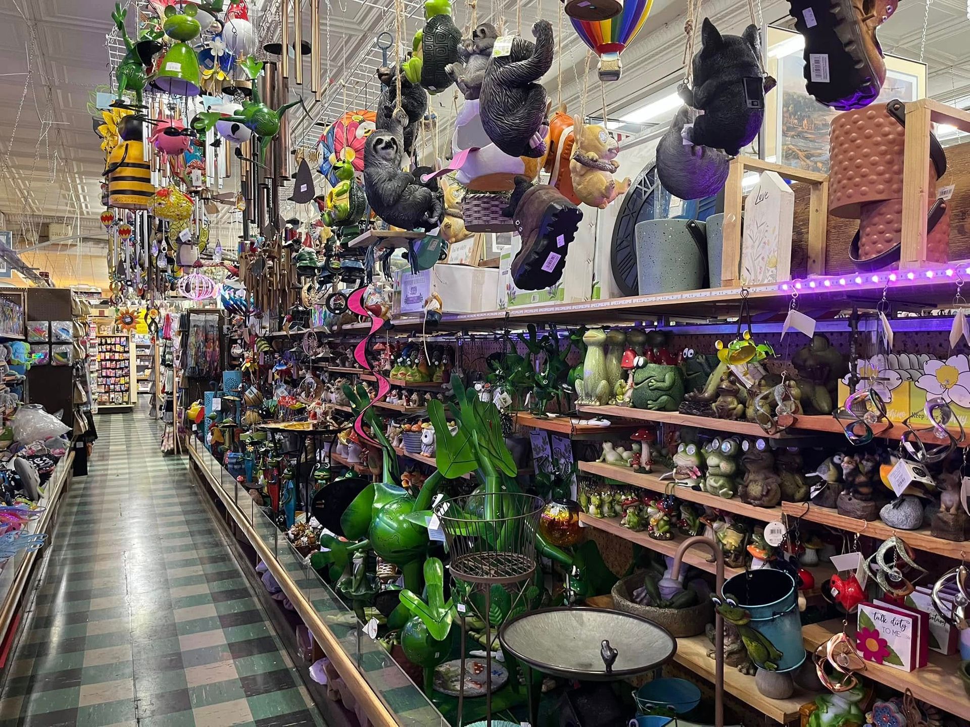A narrow shop aisle filled with shelves displaying hanging garden decor, colorful animal figurines, and patio ornaments.