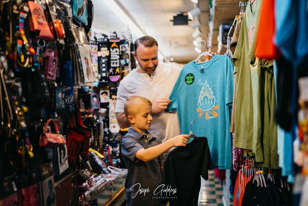 A parent and child looking at clothing inside a store. The parent holds a blue t-shirt while the child holds a black one.
