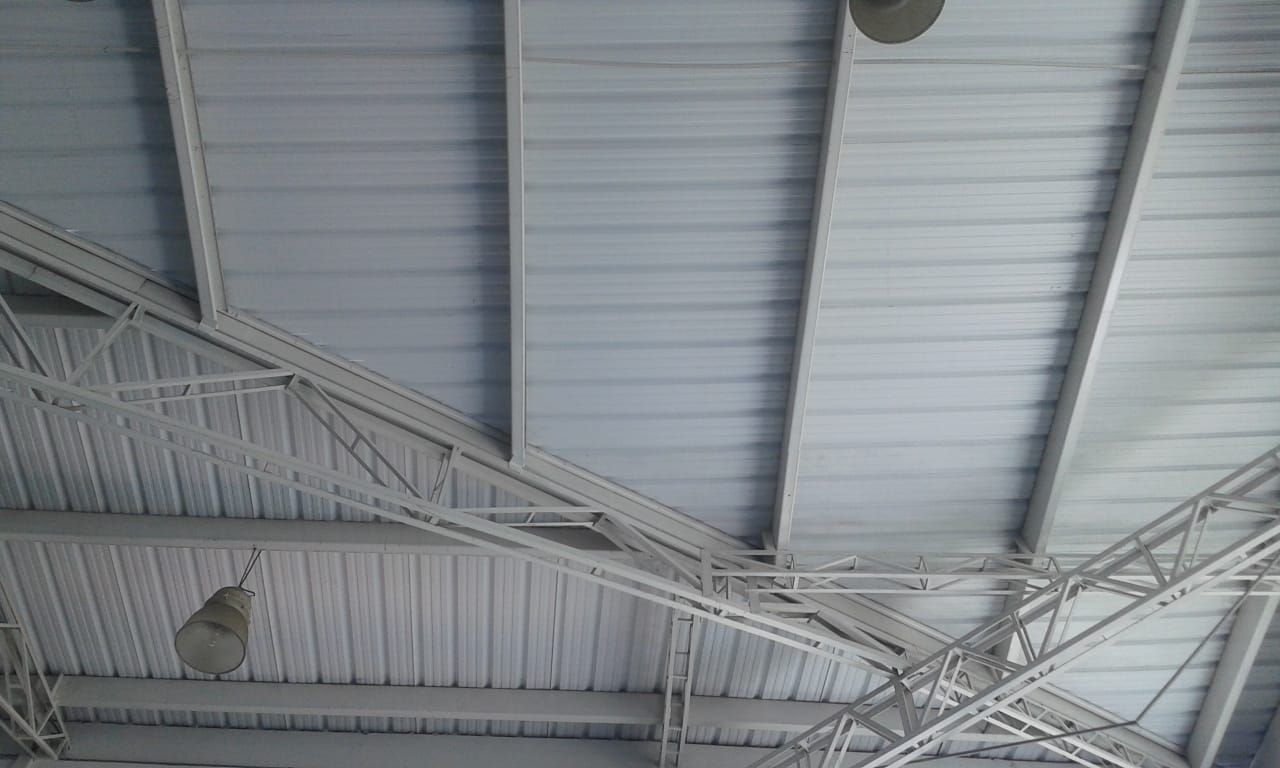 Techo de metal blanco con vigas de soporte y luces colgantes, visto desde abajo.