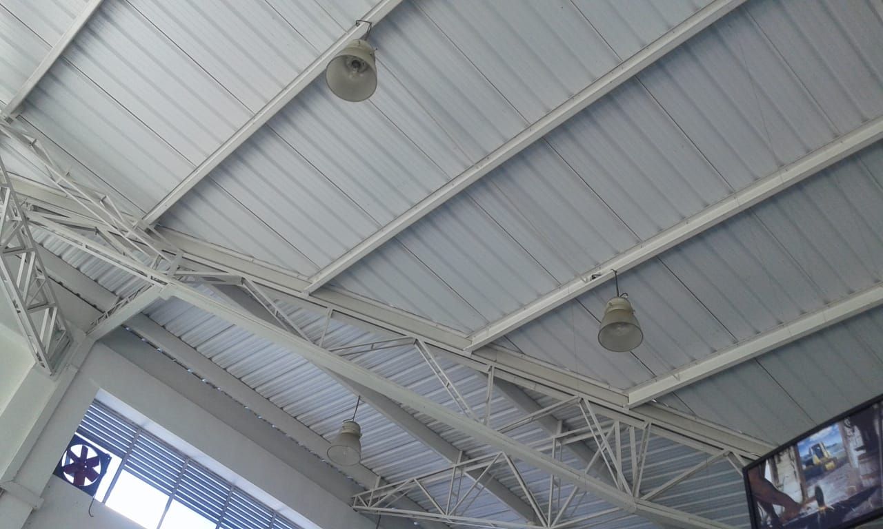 Techo de metal blanco con vigas de soporte y luces colgantes.