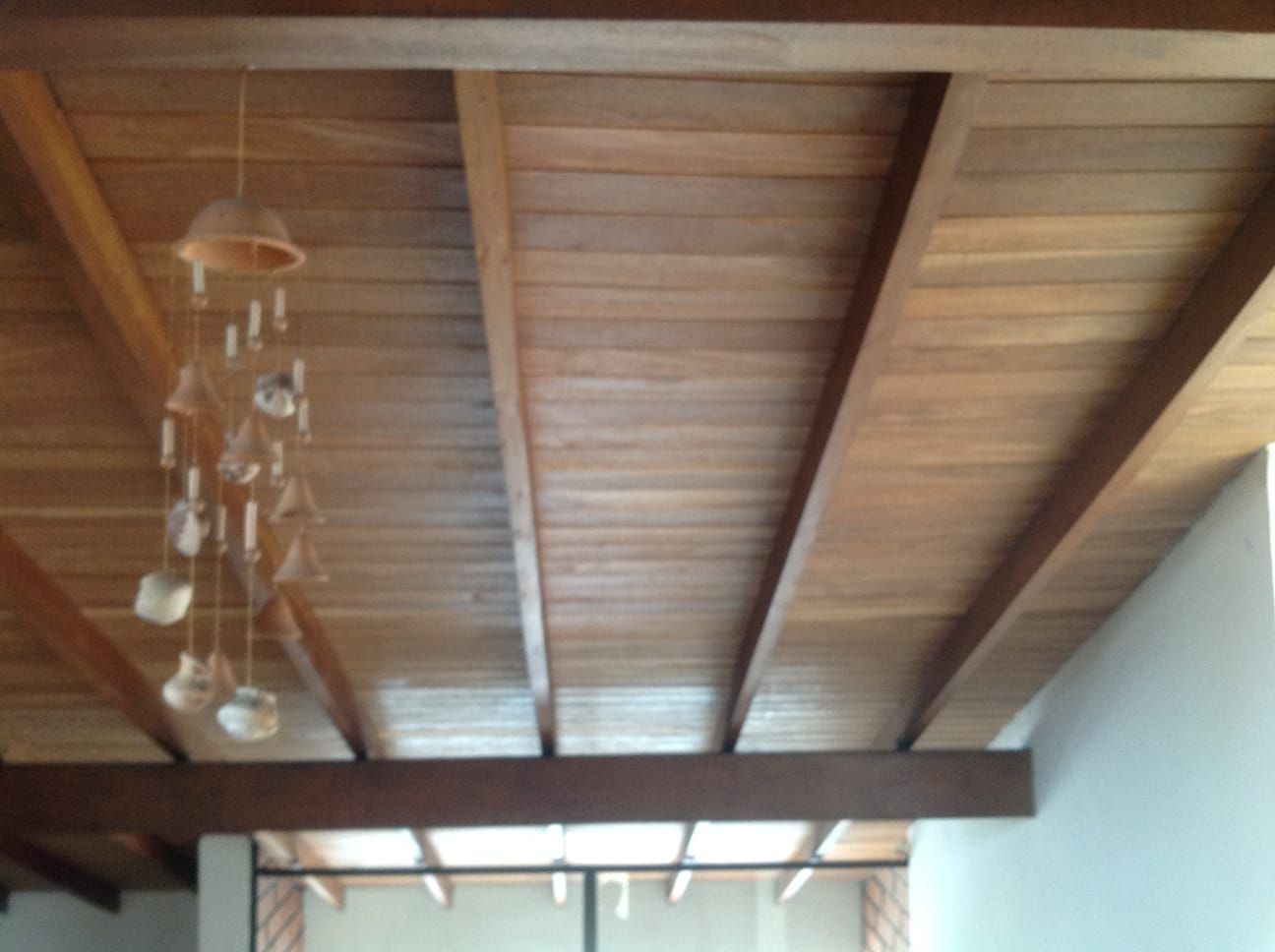 Techo de madera con vigas a la vista, pequeñas campanillas de viento colgantes, luz natural.