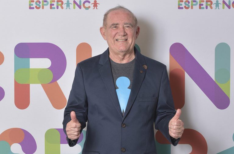 Um homem de terno faz sinal de positivo diante de uma placa que diz esperanca