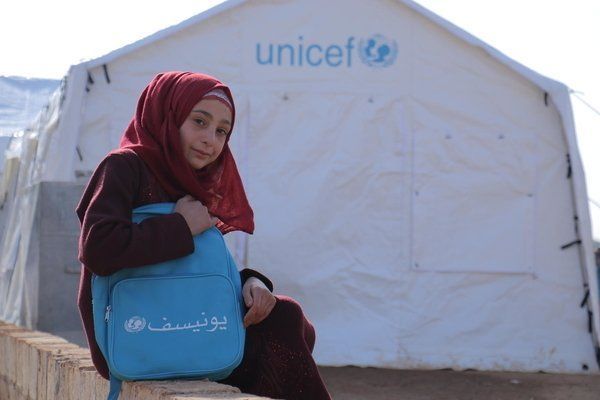 Uma garota está sentada em frente a uma tenda da Unicef