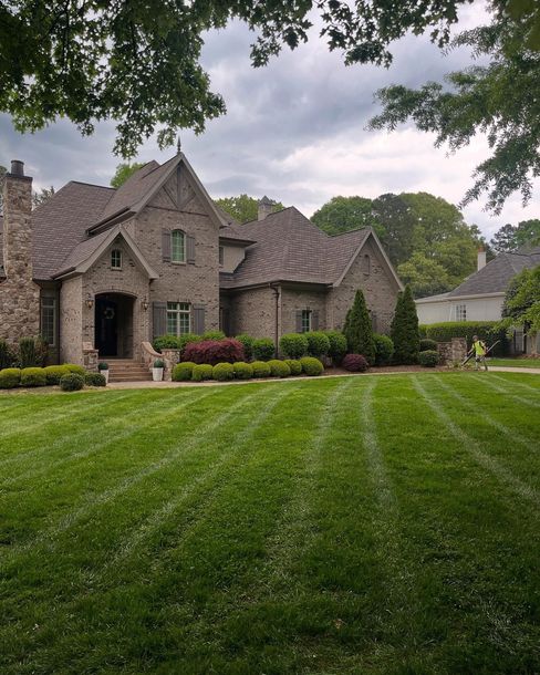 Stone house with steep gables and a large manicured lawn under cloudy skies, framed by trees