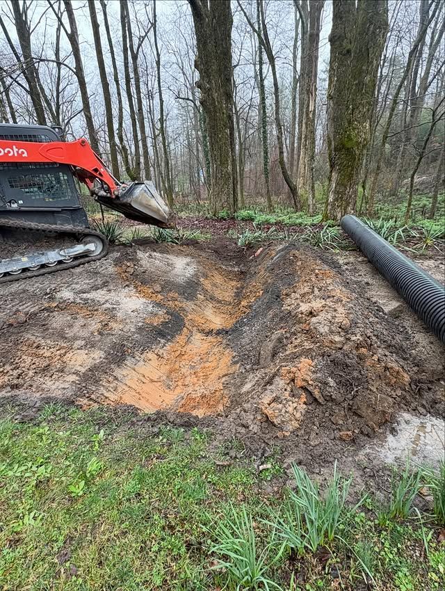 Red excavator beside muddy construction site with a large black pipe and wooded background