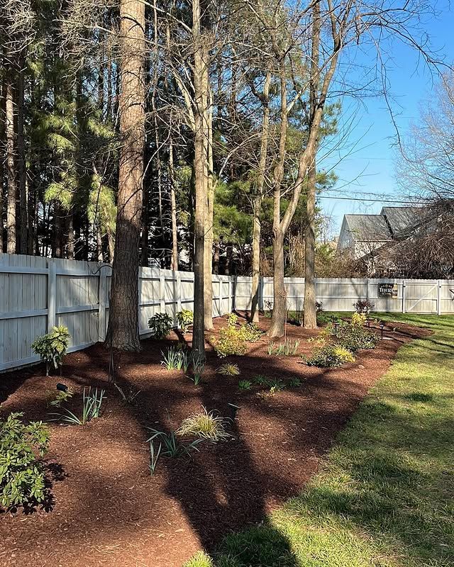 Brick house exterior with green shutters, landscaped shrubs, and a concrete walkway beside a lawn
