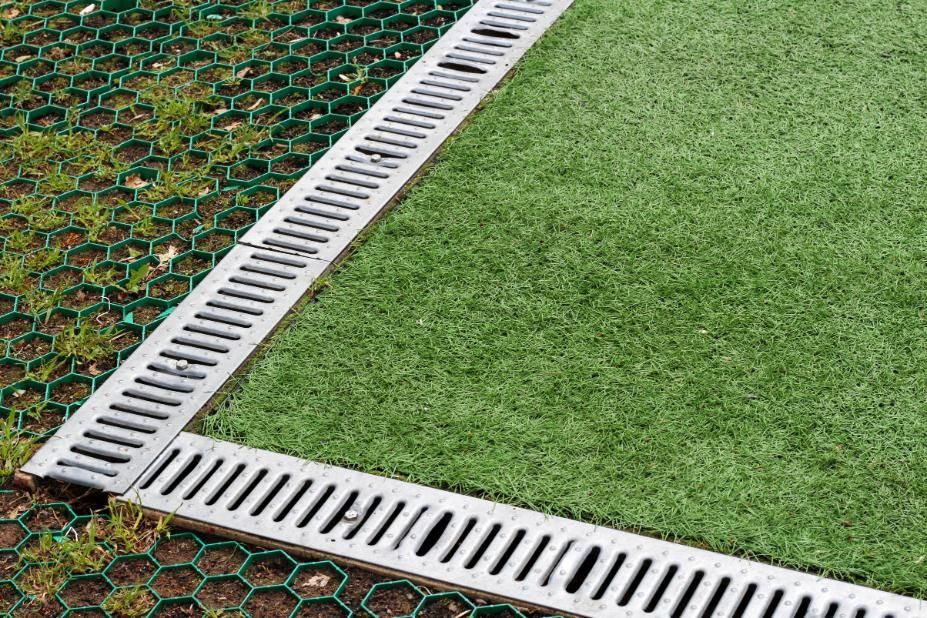 Corner of artificial turf with white drainage edging on a green and brown ground surface