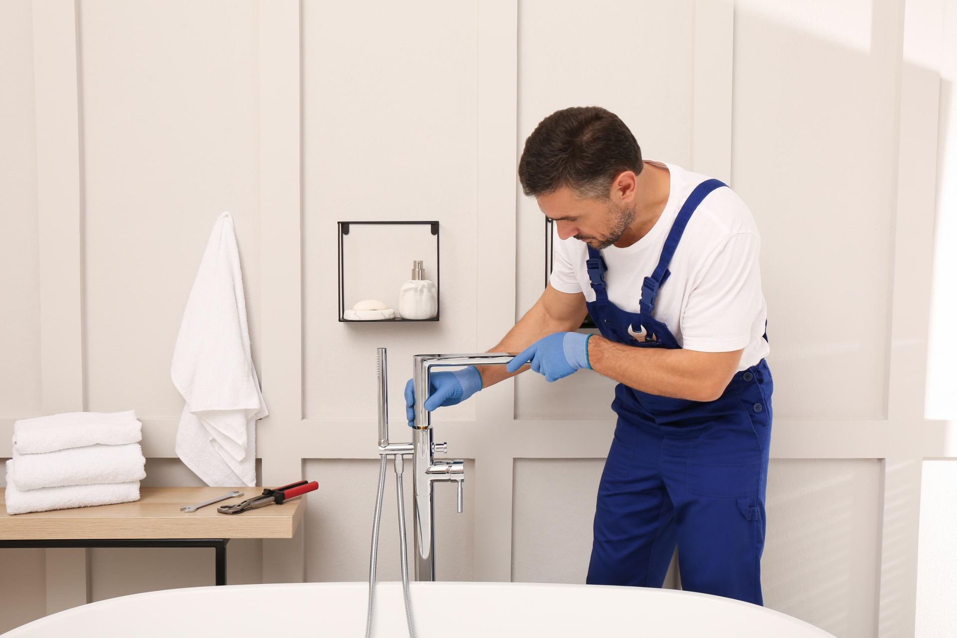 Plumber in blue overalls repairing a sink in a bright bathroom