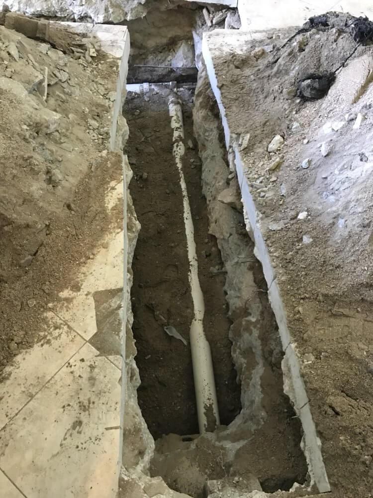 Narrow trench cut through rocky ground with a vertical pipe or conduit running down the center.