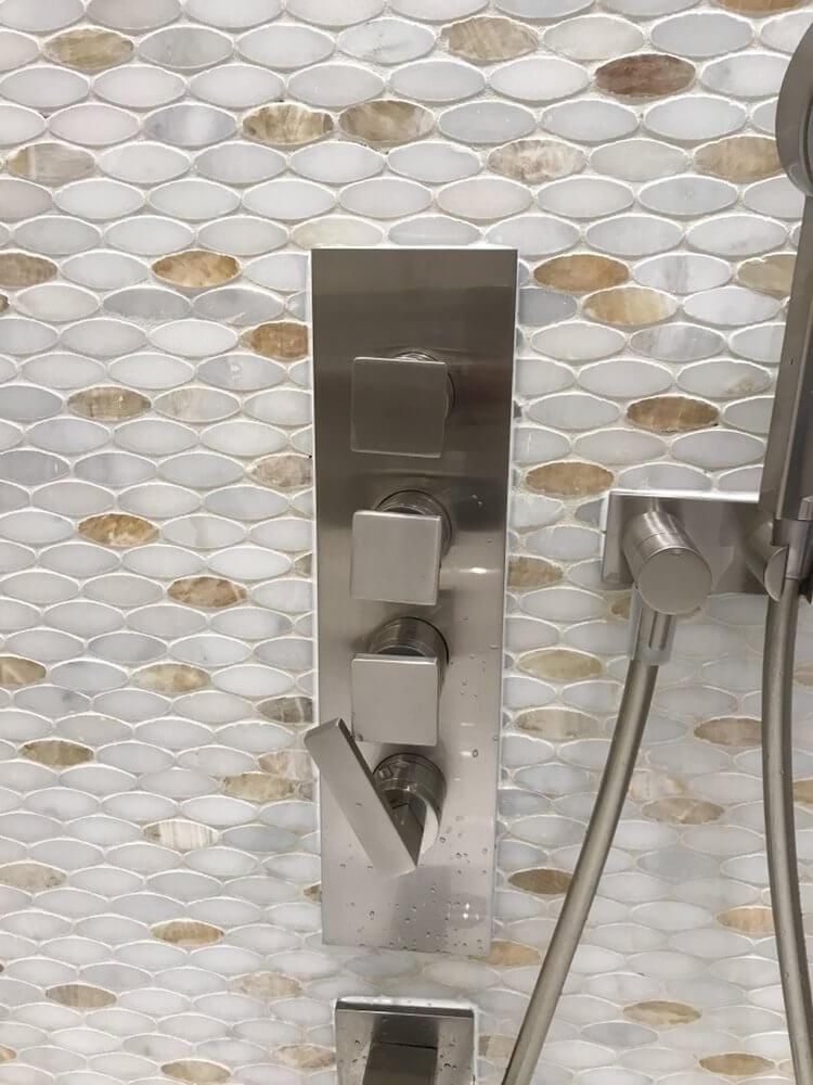 Stainless steel wall-mounted shower control against white hexagon tile