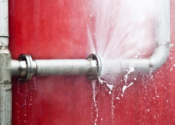 Metal pipe spraying water against a red wall, creating a splash leak