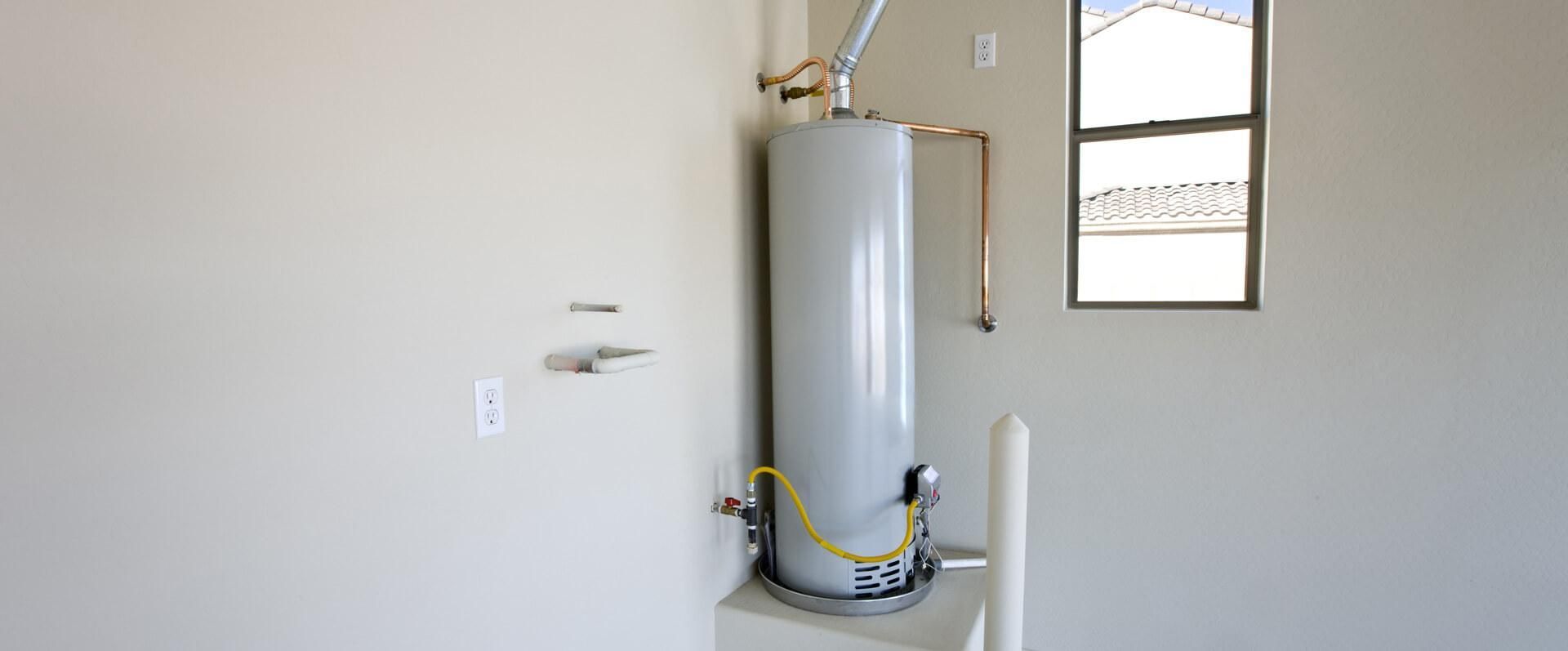 White water heater mounted on a wall with exposed pipes and valves in a utility room