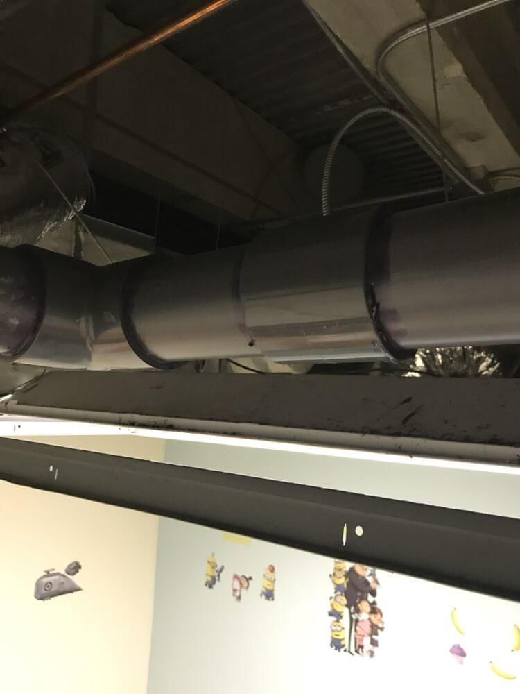 Black ductwork and ceiling pipes above a wall with small colorful stickers in a room