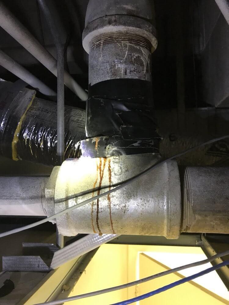Insulated HVAC ductwork and pipes in an industrial ceiling, lit by a bright work light.