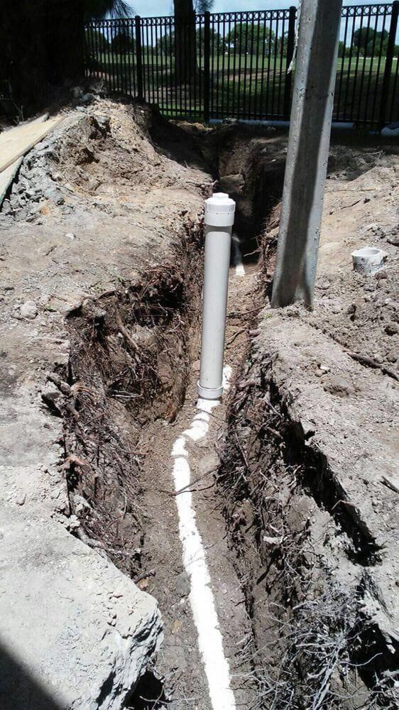 White PVC pipe installed in a trench beside a fence and utility pole during construction.
