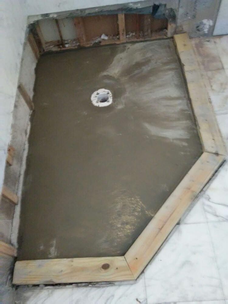 Concrete shower pan under construction with a drain in the center and wooden formwork around the edges