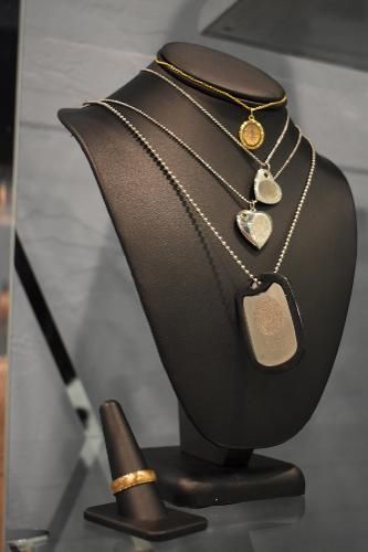 A display bust holds four necklaces featuring charms and dog tags, with a gold ring on a stand in the foreground.