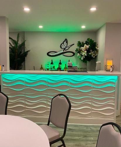 A bar with a textured, wavy white front illuminated by green LED lighting, featuring a butterfly logo on the back wall.